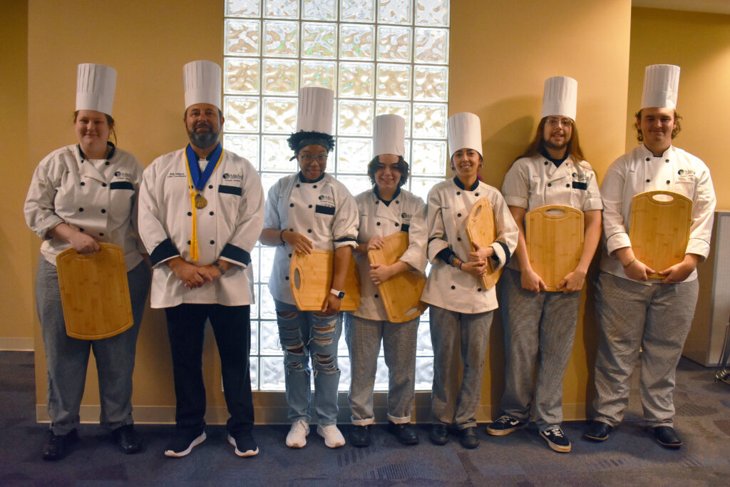 Absolwenci Mitchell Culinary Arts stoją razem do zdjęcia grupowego.